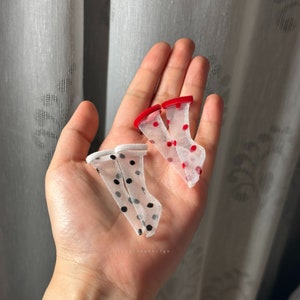 May include: Two pairs of sheer, white, polka dot socks. One pair has red polka dots and the other has black polka dots.