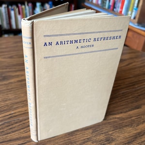 May include: A vintage book titled "An Arithmetic Refresher" by A. Hooper. The book has a tan cover with blue text and lines. The book is open, revealing the pages inside. The spine of the book also has the title printed vertically.