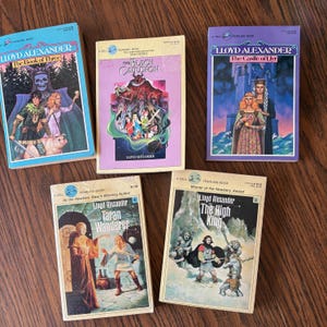 Five fantasy paperback books by Lloyd Alexander are arranged in a series. The books include "The Book of Three", "The Black Cauldron", "The Castle of Llyr", "Taran Wanderer", and "The High King".