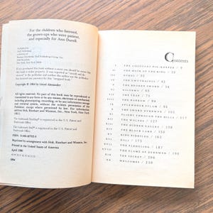 This image shows an open book with dedication text on the left page and a table of contents on the right page. The table of contents lists chapter titles and page numbers for a "The Book of Three."