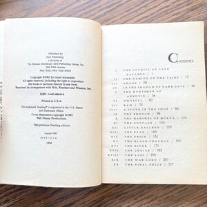 An open book, viewed from a slightly elevated angle, revealing two pages. The left page contains copyright and publication information. It lists the copyright year as 1965 by Lloyd Alexander, and states that all rights are reserved. The right page displays a table of contents. Below this heading, a list of numbered chapters is presented. The first entry is "The Council at Caer Dallben."