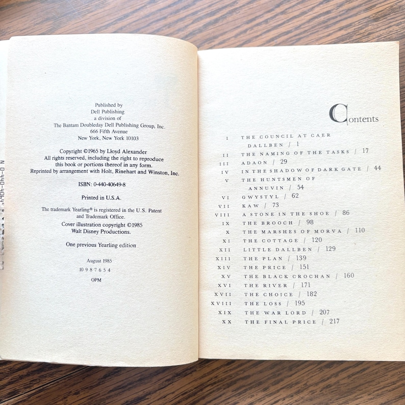 An open book, viewed from a slightly elevated angle, revealing two pages. The left page contains copyright and publication information. It lists the copyright year as 1965 by Lloyd Alexander, and states that all rights are reserved. The right page displays a table of contents. Below this heading, a list of numbered chapters is presented. The first entry is "The Council at Caer Dallben."