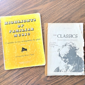 May include: Two music books. The left book is yellow with black text reading Highlights of Familiar Music, 77 melodies in easy arrangements for piano, Volume II, arranged by Denes Agay. The right book is white with black text reading The Classics.