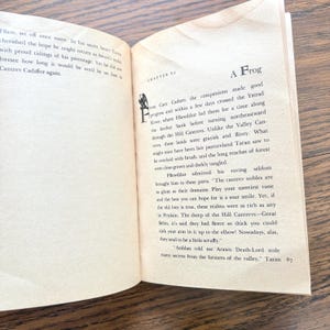 This image shows an open book with text describing Taran's journey and his companions. The right page is titled "A Frog" and features Chapter VI, detailing their progress along the Ystrad River.