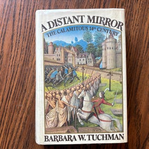 May include: A vintage hardcover book titled "A Distant Mirror: The Calamitous 14th Century" by Barbara W. Tuchman. The cover features a medieval battle scene with soldiers, a castle, and a knight on horseback. The book is on a wooden surface.