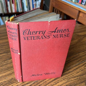 May include: A white ceramic mug with a black handle and the text "But First, Coffee" in a black, bold font. The mug is on a white surface. The mug is approximately 4 inches tall.