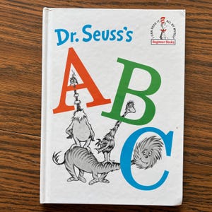 May include: A children's book titled "Dr. Seuss's ABC" with a white cover. The cover features large, colorful letters A, B, and C, with whimsical illustrations of Dr. Seuss characters. The book is part of the "Beginner Books" series.