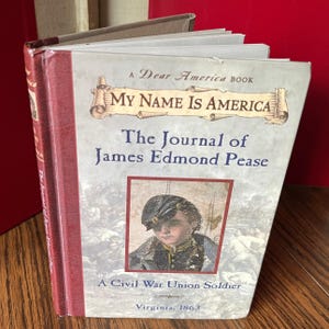 May include: A hardcover book titled "My Name Is America" from the "Dear America" series. The cover features a portrait of a Civil War Union soldier and the title "The Journal of James Edmond Pease, Virginia, 1863."