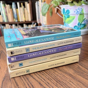 A stack of paperback books by Lloyd Alexander is displayed. The books are titled "The Book of Three," "The Black Cauldron," "The Castle of Llyr," "Taran Wanderer," and "The High King."