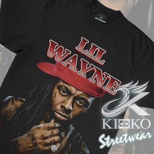 May include: Black t-shirt featuring a portrait of Lil Wayne wearing a red hat, with the text "LIL WAYNE" in red and white. The shirt also includes the "KIEKO STREETWEAR" logo.