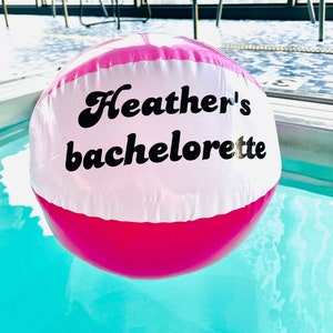 May include: A pink and white inflatable beach ball with the text "Heather's Bachelorette" printed in black.