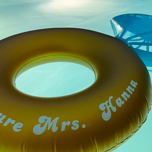 May include: A gold inflatable pool float shaped like a ring with the text "Future Mrs. Hanna" printed on it.