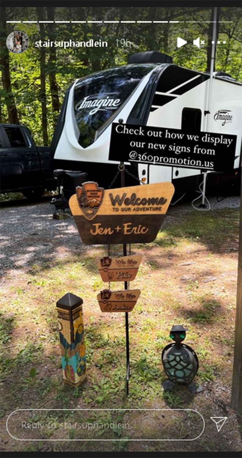 May include: A white camper with the word "Imagine" on the side, parked in a grassy area. There are wooden signs with the text "Welcome to our adventure" and "Jen + Eric".