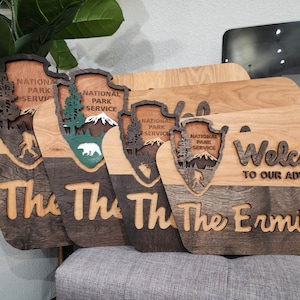 May include: Four wooden signs with a National Park Service logo and the text "The Ermitas" and "Welcome to our adventure". The signs are made of light and dark wood and have a rustic look.