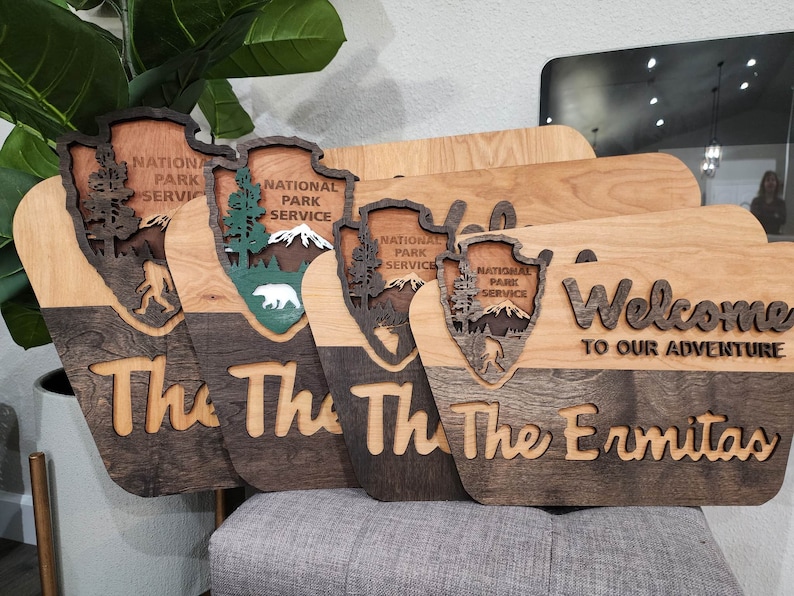 May include: Four wooden signs with a National Park Service logo and the text "The Ermitas" and "Welcome to our adventure". The signs are made of light and dark wood and have a rustic look.