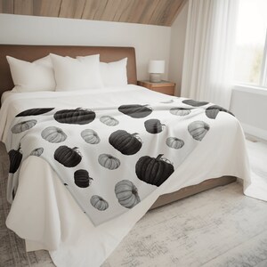 May include: A white bed with a brown headboard and a white and gray pumpkin patterned throw blanket.