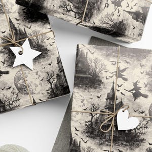 May include: Wrapped gifts with a spooky Halloween theme. The wrapping paper features a black and white illustration of a haunted house, witches, bats, and a full moon. Each gift is tied with twine and a white tag. A ball of twine, scissors, and blank tags are also present.