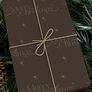 May include: A rectangular gift box wrapped in brown paper, adorned with the words "Merry Christmas" and star motifs. The box is tied with twine and set against a backdrop of green pine needles, evoking a festive Christmas theme.