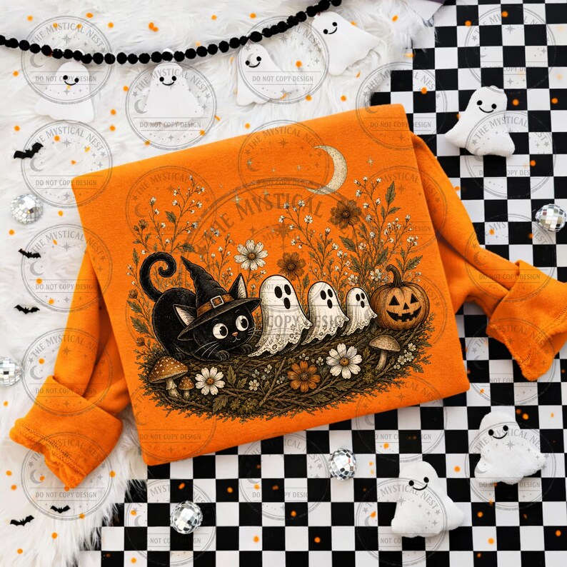 Orange sweatshirt flat lay displaying vintage Halloween cat and ghost design with pumpkin, crescent moon, wildflowers, mushrooms, and cozy spooky autumn aesthetic.