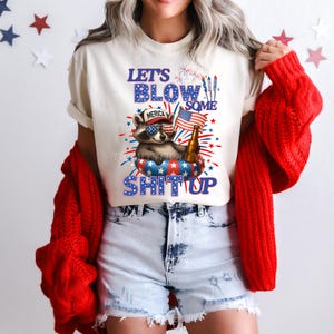 USA PNG image with a 4th of July theme digital download. The design features a cute racoon laying in a pool float holding a beer and an American flag with a hat that says merica. With red, white, and blue text that says lets blow some shit up, referring to fireworks. Same color fireworks surrounding image, perfect for Independence Day celebrations.