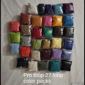 May include: A collection of twenty-seven individual square plastic bags, each containing a different colored loop of fabric. The text Pro loop 27 loop color packs is printed at the bottom of the image. The colors include white, black, purple, teal, red, brown, orange, pink, yellow, blue, green, gray, and beige.