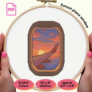 Może przedstawiać: Haft krzyżykowy przedstawiający zachód słońca widziany przez okno samolotu. Projekt przedstawia pomarańczowo-niebieskie niebo, zachodzące słońce i skrzydło samolotu. Projekt ma wymiary około 9,9 cm x 14,7 cm i wykorzystuje 16 kolorów DMC.