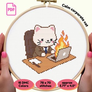 May include: Cross-stitch embroidery of a cat in a suit working on a laptop with flames, labeled "Calm corporate cat." The design is in a wooden hoop, with text indicating 15 colours, 78 x 70 stitches, and approximately 14.5 cm x 10.2 cm.
