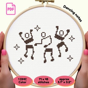 Pode incluir: Bastidor de bordado em ponto cruz com um desenho de figuras dançando e estrelas em fio marrom sobre tecido branco. O texto "Dancing notes" está no topo. O desenho tem aproximadamente 13 cm x 8 cm.