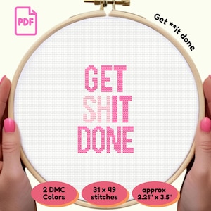 May include: A cross-stitch embroidery hoop with the phrase "GET SHIT DONE" in pink letters. The text "Get **it done" is written in the upper right corner. The design uses 2 DMC colors and measures approximately 2.21" x 3.5".