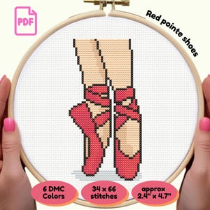 Puede incluir: Un patrón de punto de cruz de zapatillas de ballet rojas, sujetas en un bastidor de bordado de madera. El texto "Red pointe shoes" está encima del diseño. El patrón mide aproximadamente 6,1 cm x 12 cm y utiliza 6 colores DMC.