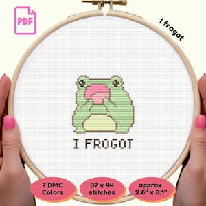 May include: A cross-stitch embroidery hoop with a green frog design and the text "I frogot". The design uses 7 DMC colours and 37 x 44 stitches, with an approximate size of 6.6cm x 7.9cm.