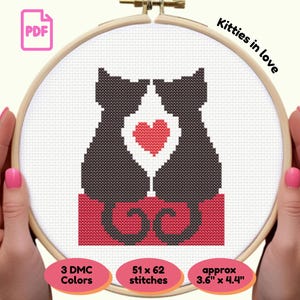 Könnte beinhalten: Kreuzstichmuster von zwei schwarzen Katzen, die sich mit einem roten Herzen dazwischen auf weißem Hintergrund gegenüberstehen. Das Design befindet sich in einem Holzreifen mit dem Text "Kitties in love". Das Muster ist ca. 9,1 cm x 11,2 cm groß.