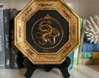 May include: Octagonal gold-framed wall decor with a black background and a gold scorpion design. The frame has intricate gold detailing and red accents. The scorpion is surrounded by a rope-like design and the word "Cancer" is written below it.
