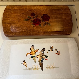 May include: Two decorative trays. The top tray is wood-toned with a red rose floral design. The bottom tray is white with a duck flying scene. Both trays have rounded edges.