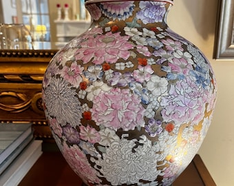 May include: A decorative ceramic lamp with a floral pattern in pink, white, purple, and red hues. The lamp has a gold-colored base and a black wooden base. The lamp is a decorative home decor item.