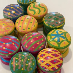 May include: A collection of 10 colorful wooden knobs with various patterns, including stripes, polka dots, and zigzags. The knobs are painted in shades of green, yellow, red, blue, and pink.