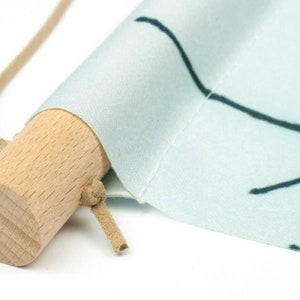 May include: A close-up of a light blue fabric wall hanging with a simple black line design. The hanging is rolled up and secured with a wooden dowel and a brown cord.