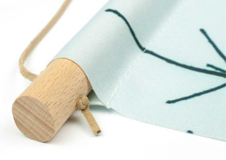 May include: A close-up of a light blue fabric wall hanging with a simple black line design. The hanging is rolled up and secured with a wooden dowel and a brown cord.