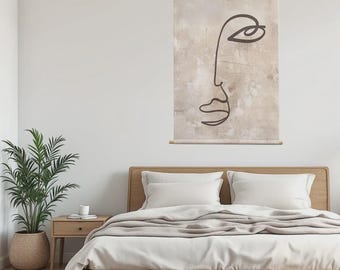 May include: A wall hanging with a minimalist line drawing of a face in dark brown against a beige, textured background. The artwork is suspended by a wooden rod and string. It hangs above a wooden bed frame with white bedding.