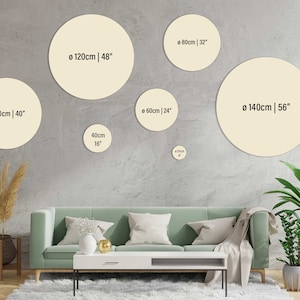 May include: A living room interior with a green sofa and a white coffee table. Five round beige wall decor pieces are displayed on the wall behind the sofa. The wall decor pieces are labelled with their diameter in centimetres and inches.