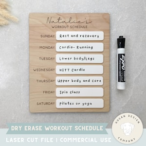May include: A wooden dry erase workout schedule board with the name "Natalie's" at the top. The board has seven days of the week listed with a blank space for writing in a workout routine. The board is designed for use with a dry erase marker, which is shown in the image.