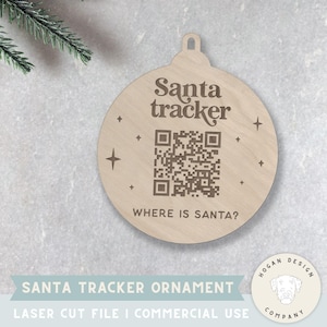 Puede incluir: Adorno navideño de madera con el texto "Santa tracker" y un código QR. El adorno también tiene el texto "WHERE IS SANTA?" y diseños en forma de estrella. El adorno es redondo con un lazo para colgar.