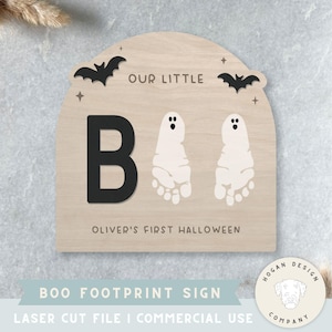 Puede incluir: Letrero de Halloween de madera con el texto "OUR LITTLE B" y "OLIVER'S FIRST HALLOWEEN". El letrero presenta una "B" negra, dos huellas de fantasmas y recortes de murciélagos. El letrero es de color madera clara.