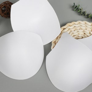 May include: Four white foam bra inserts, designed to add volume and shape to a bra. The inserts are smooth and seamless, and they are shown on a light gray background.