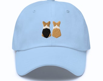 May include: A light blue baseball cap with an embroidered design of two corgis facing each other. The corgis are brown and black with white markings.