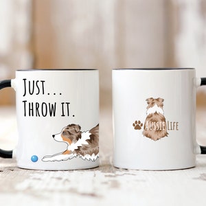 May include: Two white ceramic mugs with black rims. One mug features a brown and white Australian Shepherd dog with the text "Just... Throw It." The other mug features a brown and white Australian Shepherd dog from the back with the text "Aussie Life".