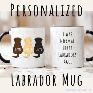 May include: White ceramic Labrador mug with black handle and rim. One side features three Labrador silhouettes in brown, yellow, and black, labeled "Coffee," "Amber," and "Onyx." The other side reads "I WAS NORMAL THREE LABRADORS AGO."