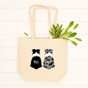 May include: A beige canvas tote bag with two black and white border collie dog illustrations. The dogs are facing away from the viewer. The dog on the left has the name "Max" printed below it. The dog on the right has the name "Ace" printed below it.