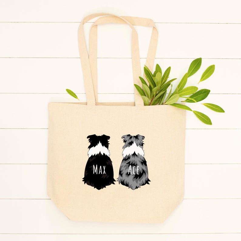 May include: A beige canvas tote bag with two black and white border collie dog illustrations. The dogs are facing away from the viewer. The dog on the left has the name "Max" printed below it. The dog on the right has the name "Ace" printed below it.