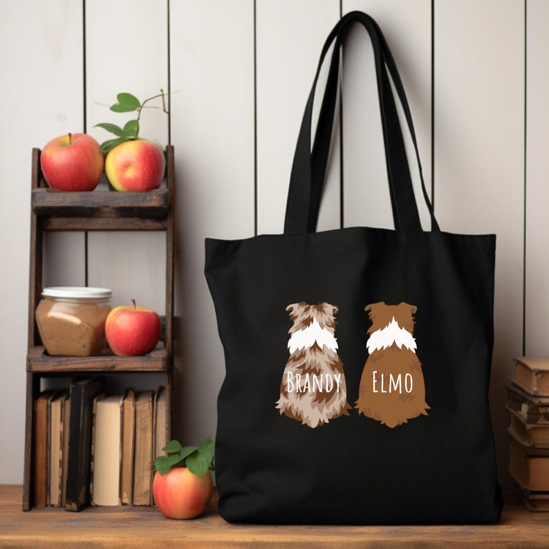 May include: Black canvas tote bag with two brown and white dog silhouettes on the back. The dogs are facing away from the viewer and the text "BRANDY" and "ELMO" is printed below each dog.